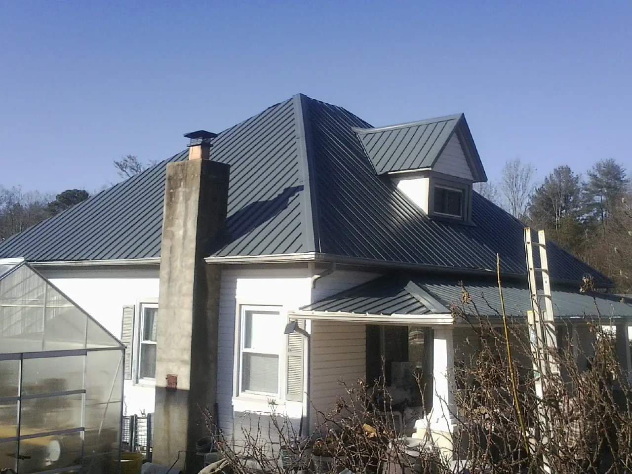 Dark blue standing seam metal roof on a white farmhouse with dormer — Slate & Tile Roof Repair by Roofing Brothers in Happy Valley
