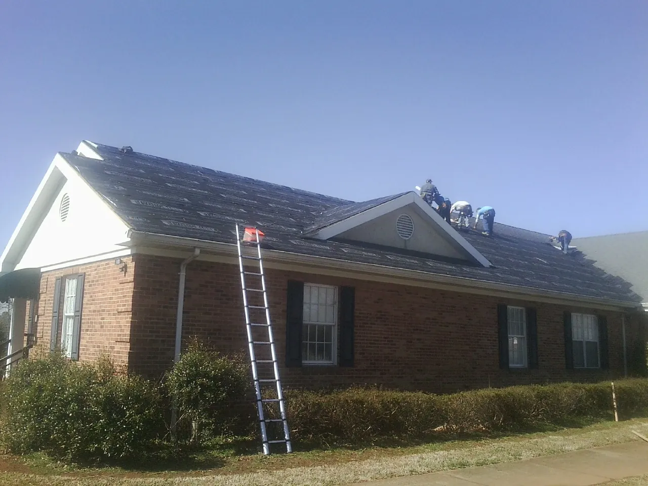 Crew tearing shingles off a brick ranch roof with a ladder set — Metal Roof Repair work by our crew in Happy Valley