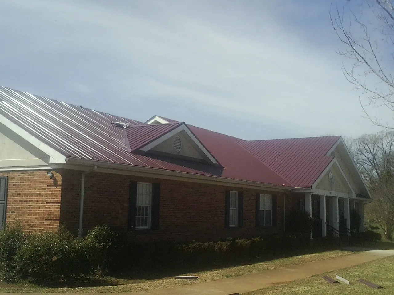 Red metal roof with gabled entries on a long brick building, from a Hail Damage Roof Repair job in Happy Valley