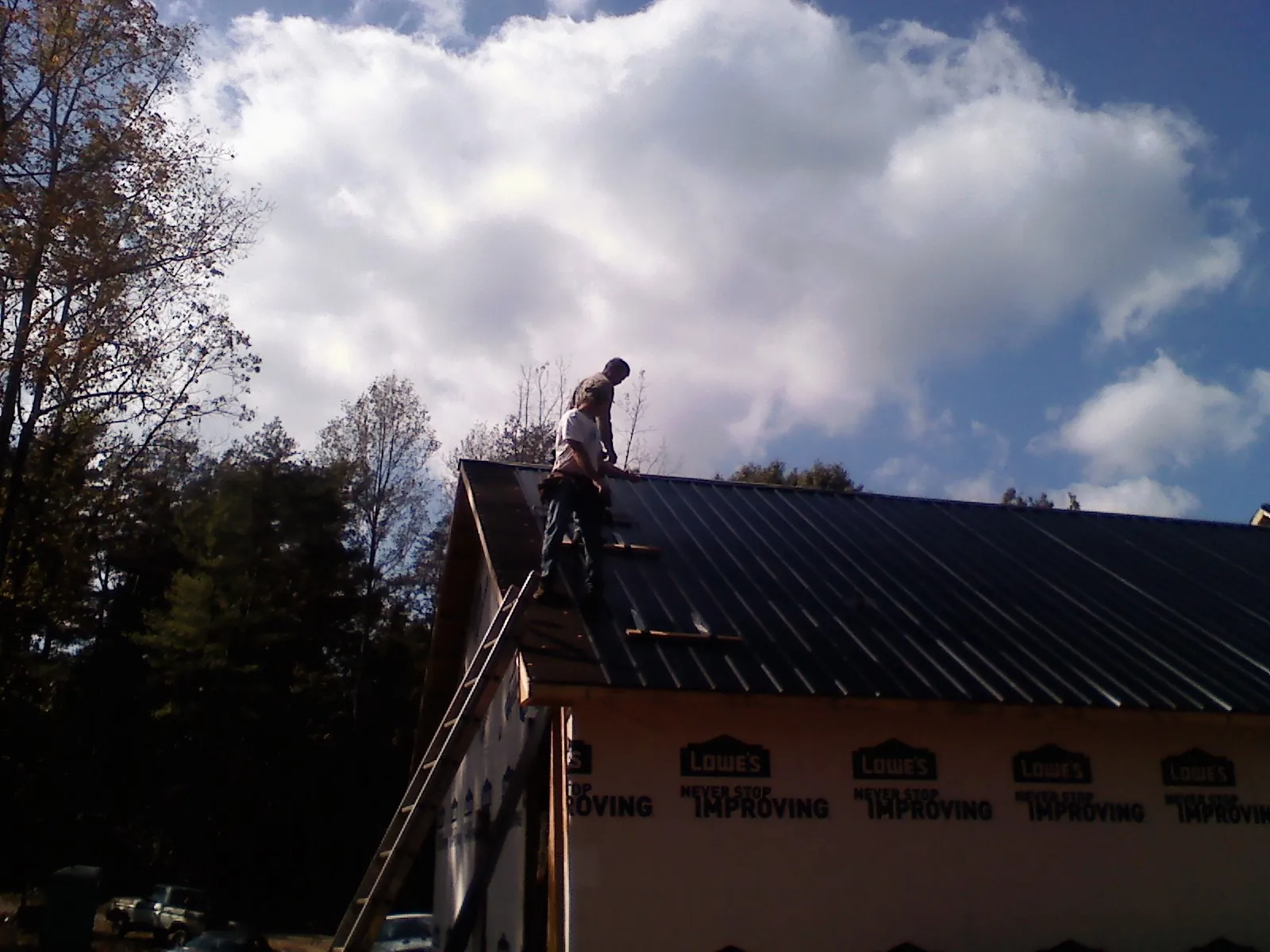 Roofer fastening dark metal panels high against a cloudy sky, from a Roof Inspection job in Happy Valley