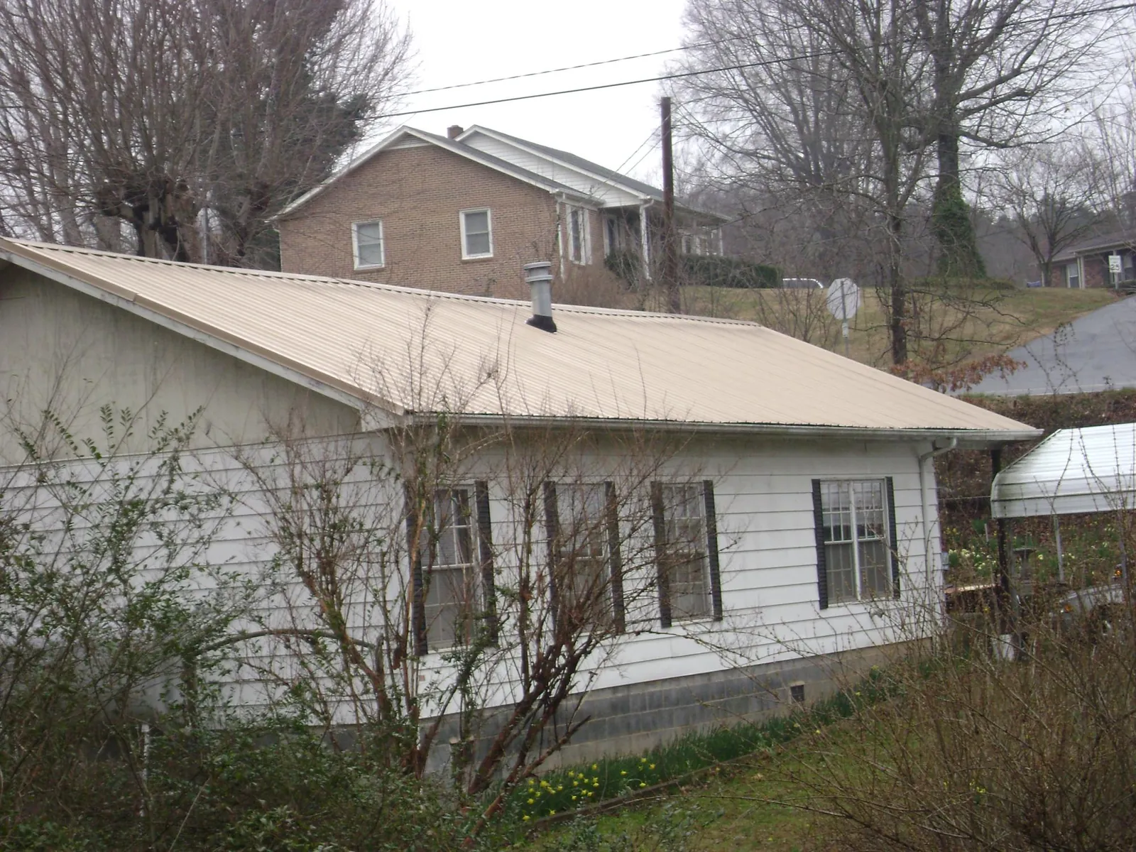 Tan metal roof on a white sided house set into a hillside — Commercial Roofing by Roofing Brothers in Happy Valley